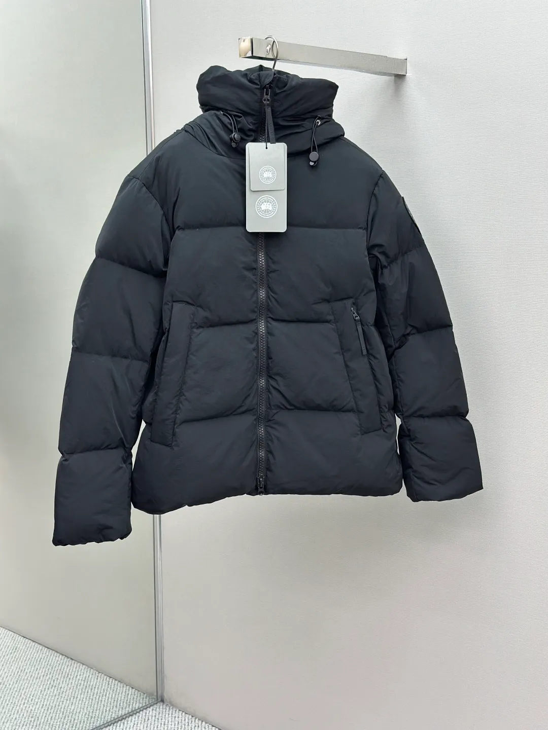 P1010 Canada Goose Black Label Badge Hooded Down Jacket (khaki) The high-quality filling is made of 90 national standard high-quality white duck down, selected high-loft velvet, weighing 240g, light and warm, with excellent temperature locking performance and good resilience. The fabric is woven with 400T high-count yarn. After special water-repellent treatment, the surface forms a lotus leaf effect - raindrops will slide down like beads, and snow particles will fall off when touched. The tear resistance reaches 200N (approximately 20kg load-bearing), the light gray matte texture breaks the stereotype of "outdoor clothing = hardcore", and the soft luster presents a high-end matte effect under urban neon lights, seamlessly switching scenes from ski resorts to CBD office buildings. The ribbon is woven with polyester as the base, and the brand letters are decorated on the ribbon through high-precision computer embroidery. The edges of the pattern are clear, the stitches are fine and even, and multiple layers of embroidery thread are stacked to enhance the three-dimensional effect. Precision thread reinforcement prevents linting and ensures the fluffy and resilient elasticity lasts as new. The embedded cuffs are three-dimensionally woven to form a "wavy" elastic structure, which forms natural folds when fitting the wrist, increasing the contact area with the skin, thus improving the windproof effect. At the same time, micro-velvet treatment is added to the inside of the cuffs, which feels like a second layer of skin and avoids friction on the skin from metal zippers or hard fabrics. Size:S-M-L-XL